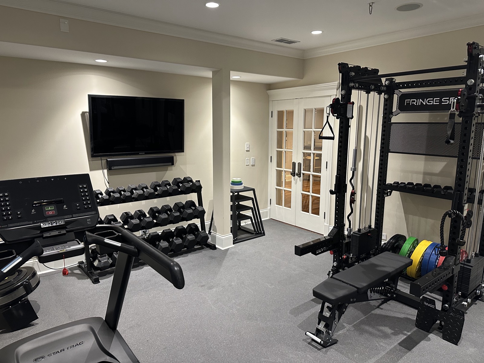 Fully equipped basement home gym with Fringe Sport rack and Star Trac treadmill sourced by CS Gym Design